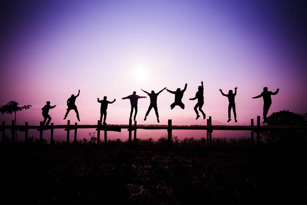 Silhouet van Jumping team / vrienden springen op de houten brug op heuvel - gelukkig en grappige genieten van springen van mensen met de zonsopgang of zonsondergang in vakantie - Foto, afbeelding