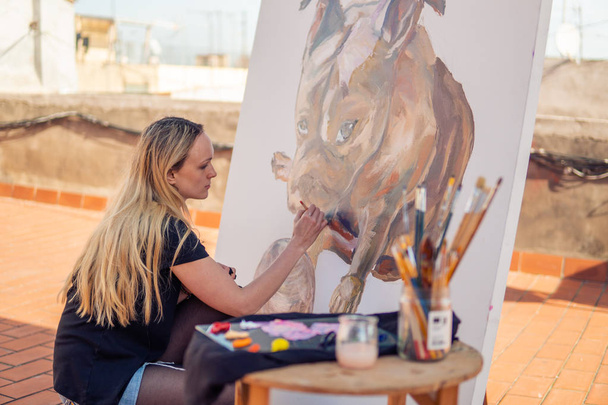 junge Frau malt Künstler Zeichnung zu Hause Dach. Bild einer Bulldogge auf großer Leinwand. Kunst im Freien - Foto, Bild