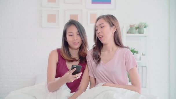 Young Asian women lesbian happy couple using phone VIDEO Call with friend in bedroom at home, couple enjoy love moment while lying on bed when relaxed. Lifestyle LGBT couple together indoors concept. - Video