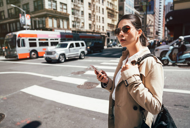 Asian female tourist using phone app to find directions and guide during travel san francisco usa. Happy Chinese woman in sunglasses texting on mobile sms smartphone standing on zebra crossing road - Valokuva, kuva