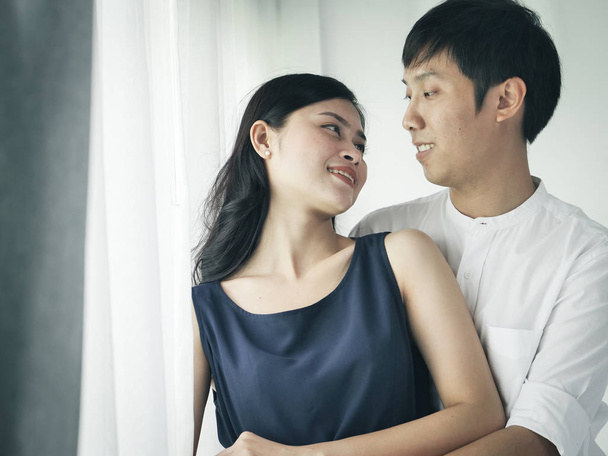 Romantic Asian couple hug and kissing near window at home, lifestyle concept. - Фото, зображення