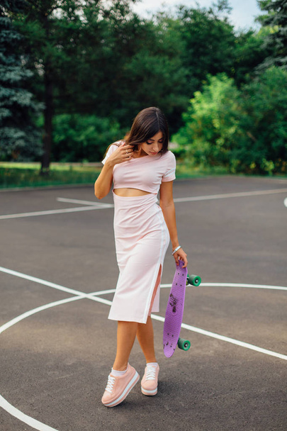 Portrait of a smiling charming brunette female holding her skateboard on a basketball court. - Foto, immagini