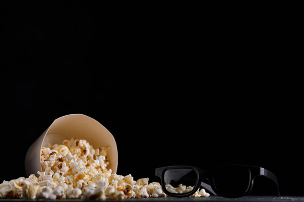 Snack for watching movies. Bucket with popcorn on a black background and glasses. Close-up. - Φωτογραφία, εικόνα