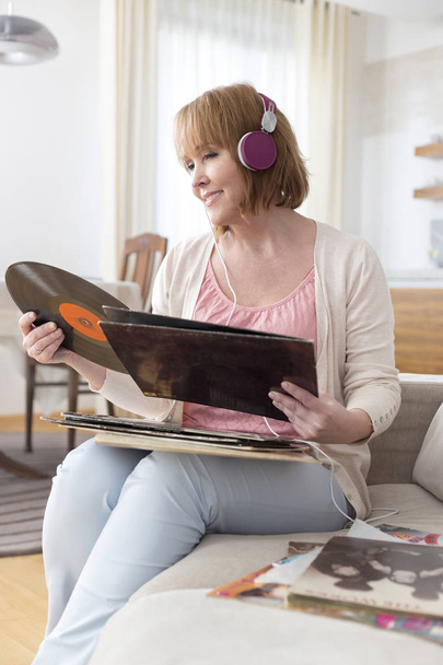 Mature woman looking at record while listening music in living room - Zdjęcie, obraz