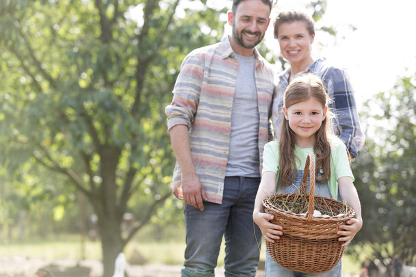 Parents standing with girl holding eggs in basket at farm - Foto, Bild