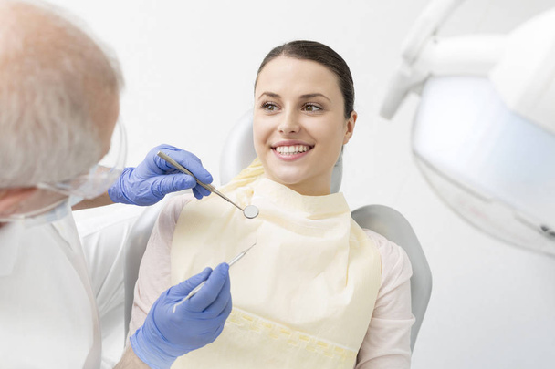 Senior dentist examining young patient with dental equipment at clinic - Φωτογραφία, εικόνα