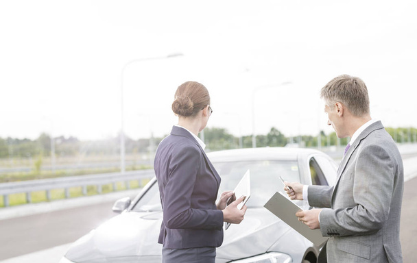 Insurance agent discussing with businesswoman while pointing at breakdown car against sky - Fotoğraf, Görsel