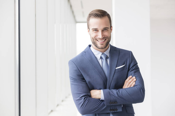 Portrait of smiling handsome young businessman standing with arms crossed in new office - Fotografie, Obrázek