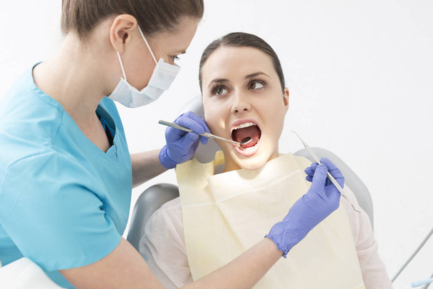 Dentist examining patient mouth with angled mirror and scaler at dental clinic - Foto, Bild