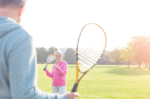 Uśmiechnięta kobieta senior serwujemy badmintona w parku - Zdjęcie, obraz
