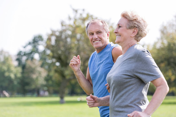 Happy senior man looking at woman while jogging in park - Фото, изображение