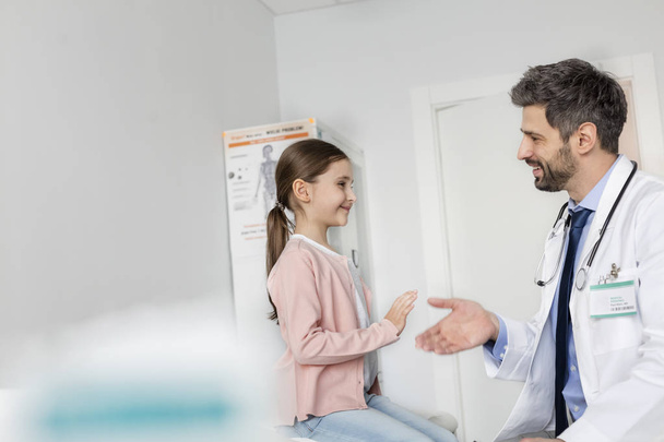 Smiling mid adult doctor shaking hands with girl patient at hospital - Foto, Imagen