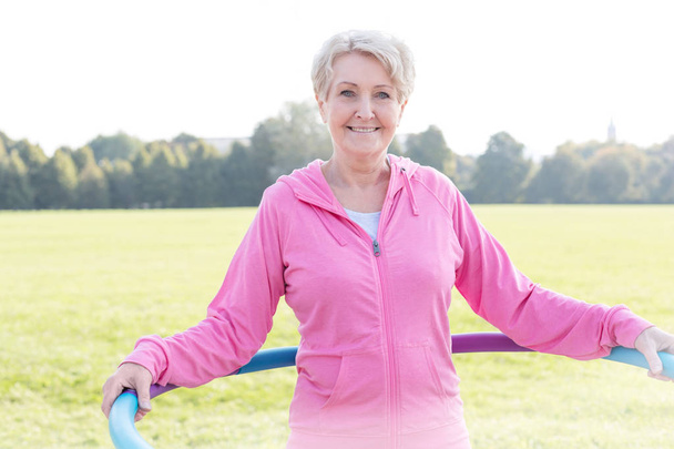 Senior woman exercising with hula hoop in park - Photo, Image