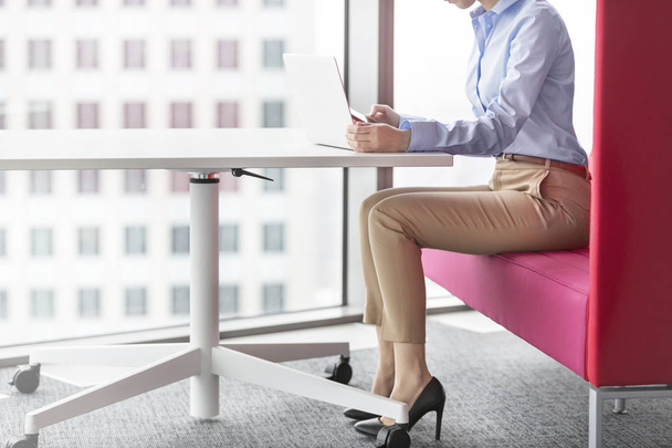 Low section of businesswoman using laptop while sitting at office - Foto, afbeelding