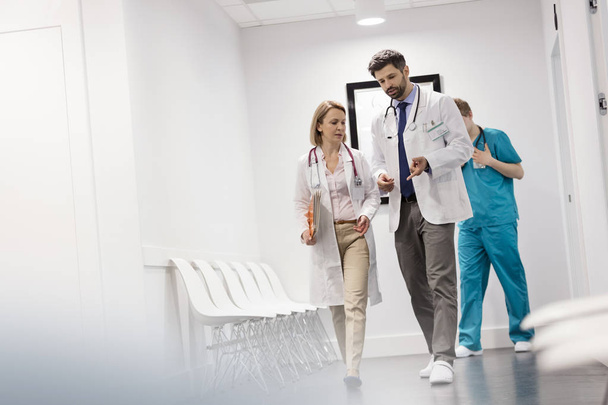 Nurse walking behind doctors discussing at corridor in hospital - Valokuva, kuva