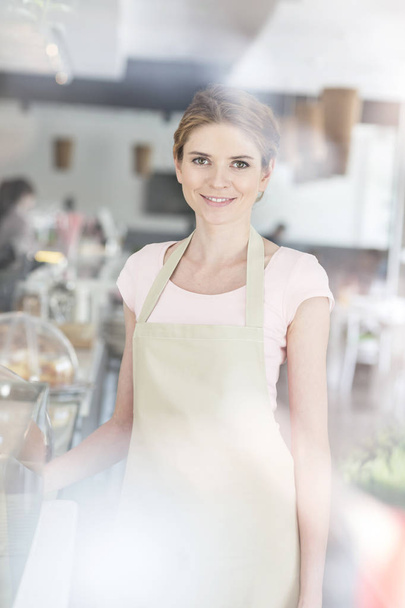 Portrait of smiling beautiful young waitress standing by counter at restaurant - Foto, Bild