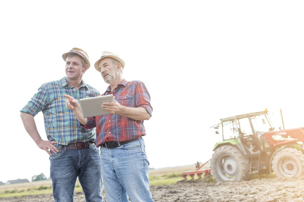 Farmers with digital tablet discussing on field against sky at farm - 写真・画像