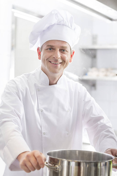 Portrait of smiling chef with steel cooking pot in kitchen at restaurant - Foto, immagini