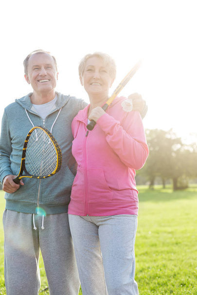 Happy senior couple holding tennis bats in park - Fotó, kép