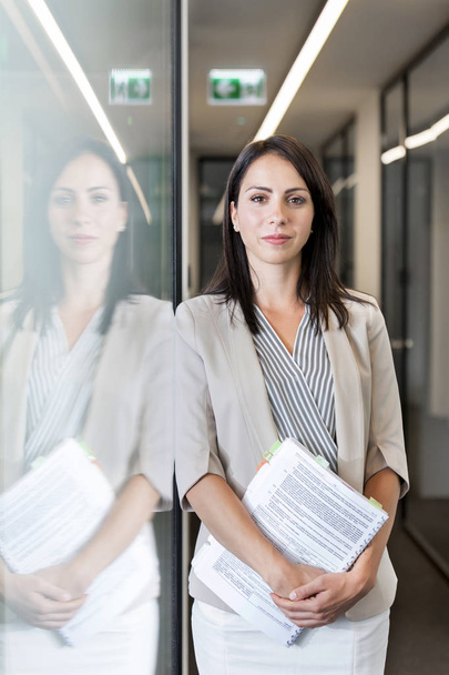 Portrait of confident businesswoman standing with documents at office - Valokuva, kuva