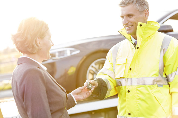 Smiling tow truck driver giving car key to businesswoman - Valokuva, kuva