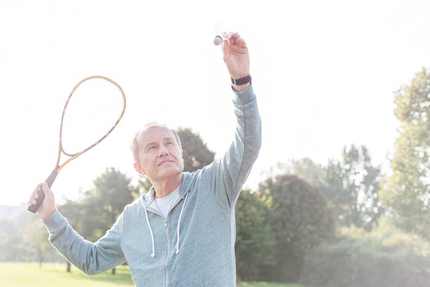 Confident senior man serving badminton in park - Photo, Image