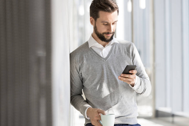 Businessman texting on mobile phone while having coffee at office - Foto, Bild