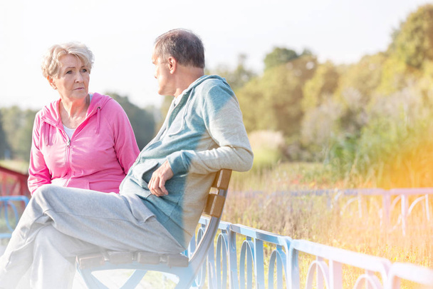 Active senior couple talking while resting on bench at park - Photo, Image
