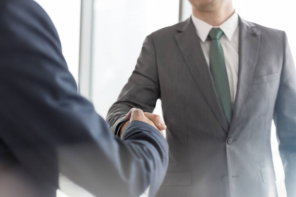 Midsection of businessmen shaking hands while standing in boardroom during meeting at office - Photo, image