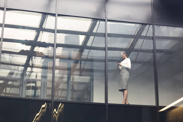 Niski kąt widzenia bizneswoman stoi przez okno w biurze - Zdjęcie, obraz