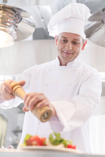 Confident chef using pepper mill on salad in plate at restaurant - Foto, imagen