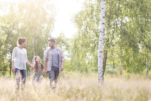 Menina sorrindo andando com os pais contra as árvores no campo
 - Foto, Imagem