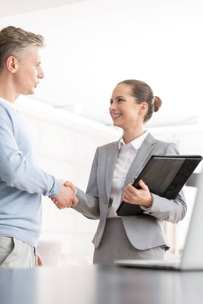 Smiling mature man and saleswoman shaking hands in apartment - Foto, Bild