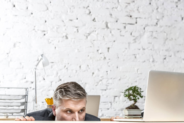 Mature businessman looking at laptop on desk against brick wall - Foto, imagen