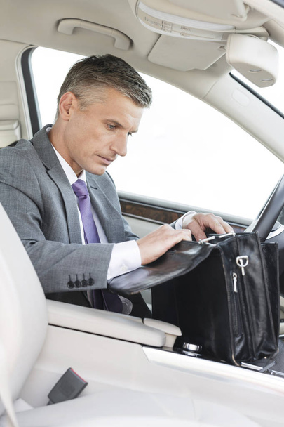 Businessman searching in bag while sitting in car - Zdjęcie, obraz