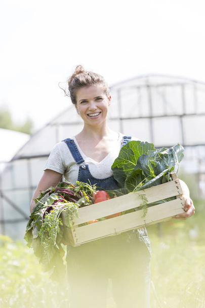 Portrait of smiling adult farmer holding vegetable crate at farm - Fotografie, Obrázek