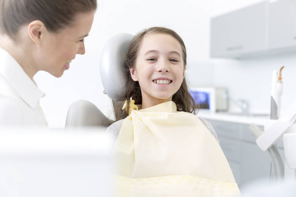 Dentist looking at smiling patient sitting in dental clinic - Photo, image