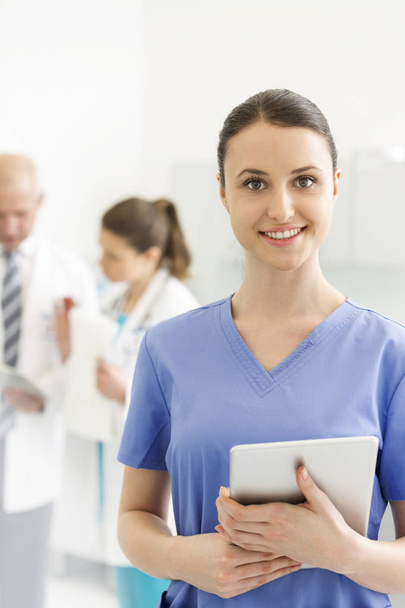 Portrait of nurse with digital tablet standing against doctors at clinic - Photo, image