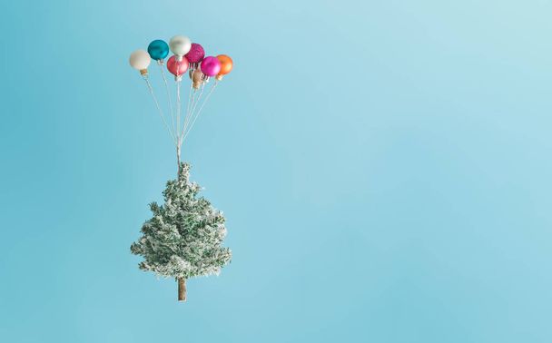 Weihnachtsbaum, der von bunten Luftballonornamenten vor himmelblauem Hintergrund in die Höhe gehoben wird. Neujahrskonzept. - Foto, Bild