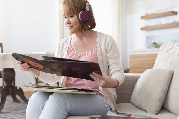 Mature woman looking at record while listening music in living room - Fotó, kép