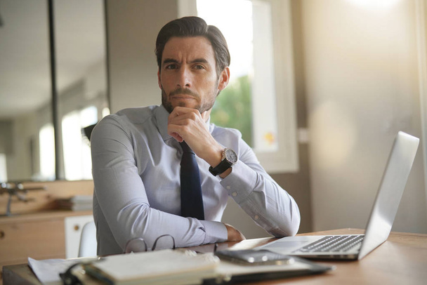 Smart handsome businessman in office with laptop looking at camera - Photo, image