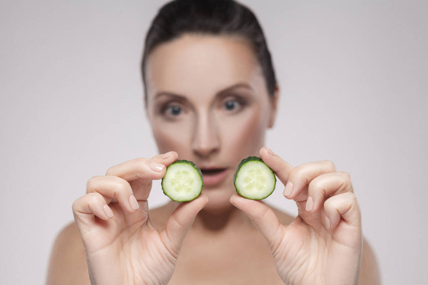 healthy middle aged holding slices of cucumber on grey background - Zdjęcie, obraz