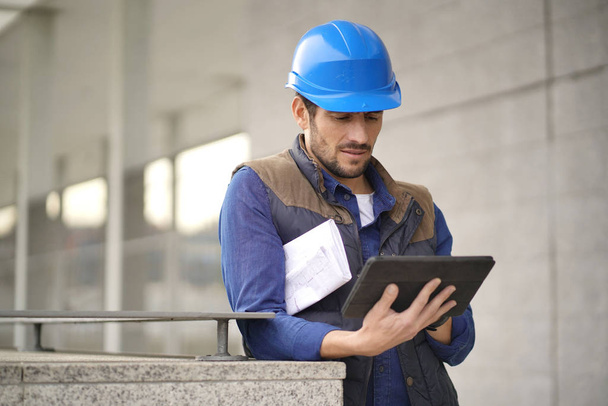 Handsome building expert in hardhat outdoors with tablet and blueprint - Valokuva, kuva