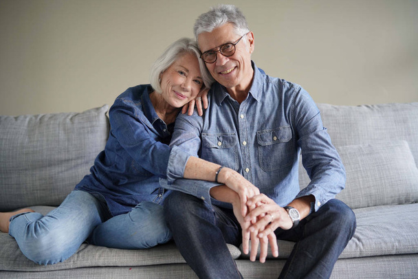 Modern senior couple in denim on couch looking at camera                                - Photo, Image