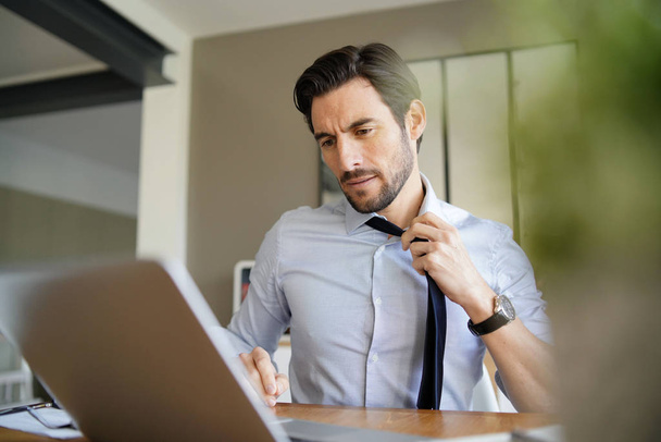 Relaxed attractive businessman undoing tie and working in modern office - Photo, Image