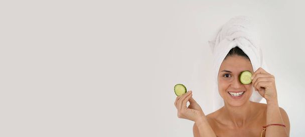 Stunning natural beauty in towel turban smiling with cucumber slices - Fotó, kép