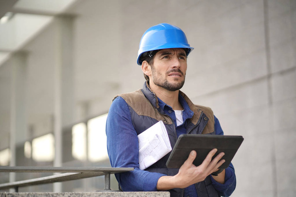 Handsome building expert in hardhat outdoors with tablet and blueprint - Fotó, kép