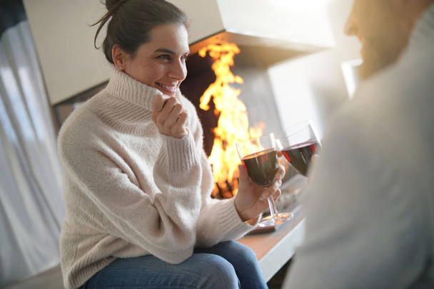  Couple relaxing by the fire enjoying glasses of red wine                               - Фото, изображение