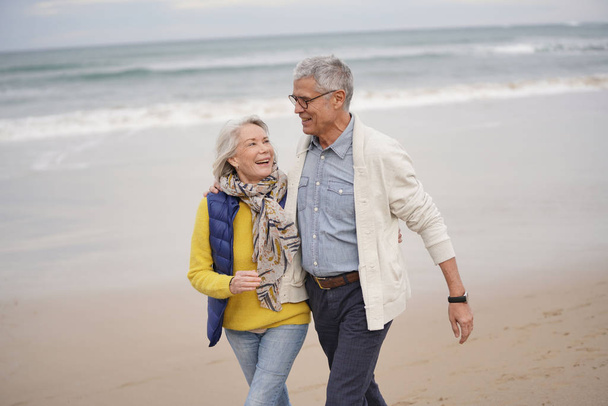  Happy senior couple walking together on the beach                               - Valokuva, kuva