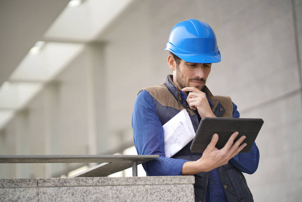 Handsome building expert in hardhat outdoors with tablet and blueprint - Photo, Image